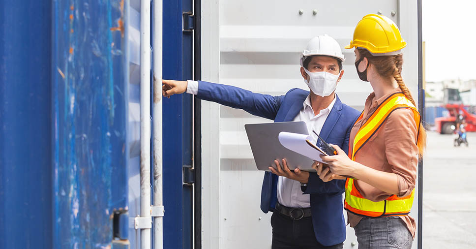 dois engenheiros equipados com capacete, máscara tendo ajuda da prancheta e notebook para fazer a gestão de obras